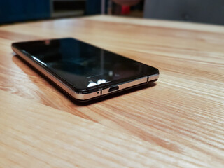 Black modern smartphone with blank screen on wooden surface. Selective focus.