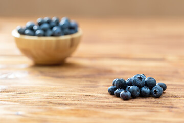 Pile of fresh blueberries with full wooden bowl on desk. Lots of sweet healthy berries on wooden table. Heap of little nutritious raw fruit with woody dish with bilberries.