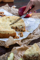 Close up of a hand with knnife cutting delicious apple pie on wooden background