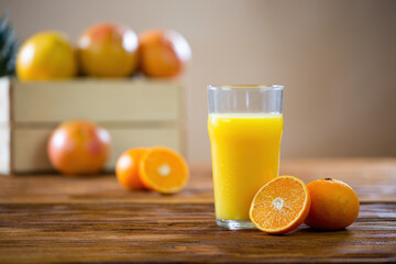 Orange cut in half lying on a wooden table next to glass of freshly squeezed juice. Yellow liquid from fruit with brown box in background. Concept of healthy eating.