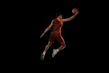 Flying. Young purposeful african-amrican basketball player training, practicing in action, motion isolated on black background. Concept of sport, movement, energy and dynamic, healthy lifestyle.