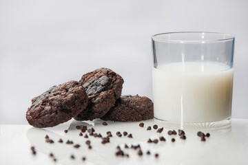 Stack of round chocolate chip cookies and glass of milk on reflective surface over white background