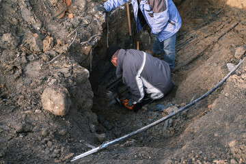 Man cuts thick electric wire in a trench in the ground.