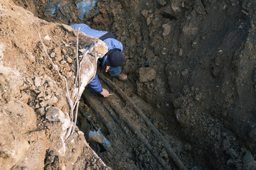 Fototapeta premium An electrician checks old electrical wiring in a trench in the ground