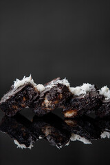 Brownies decorated with coconut flakes on reflective black surface over dark background