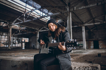 Fototapeta na wymiar Young Girl Playing Guitar in an Abandoned Hall