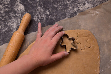  Hands carve gingerbread cookies with festive metal cutters. Making gingerbread from raw dough