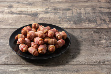 Obraz premium Pig in blankets. Sausages wrapped in smoked bacon on wooden table 