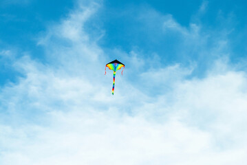 Rainbow color bright kite toy flying high up in blue sky background