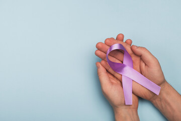Man holding lavender color awareness ribbon on light blue background. World cancer day, epilepsy....
