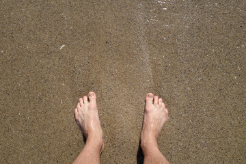 Man's feet from top and sea sand.