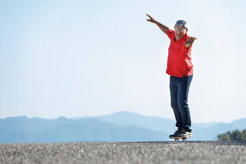 Uomo settantenne con polo rossa, va nel suo skateboard stando in equilibrio in una strada di...