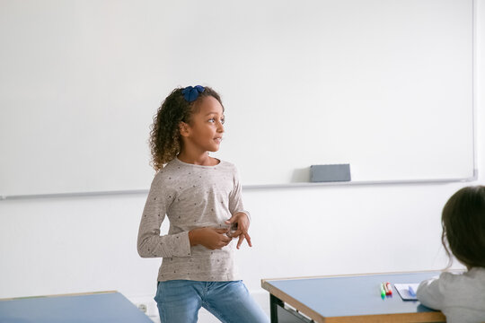 Pensive smiling African American schoolgirl standing at whiteboard in front of class. looking away at window. Copy space. Education or back to school concept