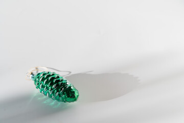 Green pine cone glass vintage christmas bauble on white background with sunlight and shadow