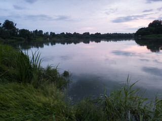 Landscape of Sava river in Poloj near Bosanski Brod, Bosnia and Herzegovina with green grassy and forested shore, calm water with reflection and beautiful clouds in sky during evening in summer