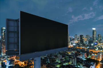 Blank black road billboard with Bangkok cityscape background at night time. Street advertising poster, mock up, 3D rendering. Side view. The concept of marketing communication to promote idea.