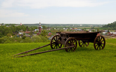 Wooden vintage cart stands on green grass against the background of the old city. Selective focus, background blur.
