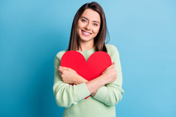 Photo of lovely young girl cuddle red paper heart figure toothy smile wear green sweater isolated blue color background