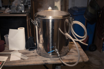 Stainless steel brewing keg and other micro brewery equipment on wooden table in garage