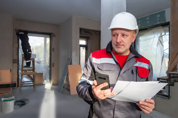 Builders inside a building under construction. An engineer with a phone and drawings is standing on...