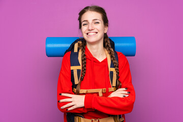 Young mountaineer girl with a big backpack over isolated purple background laughing