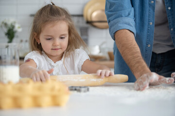 Caring young Caucasian father and cute little preschooler daughter bake in kitchen at home together