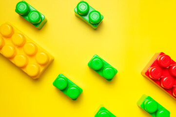 Multicolored plastic kids constructor on yellow background. Colored children's bricks for construction. Flat lay top view copy space. Plastic building blocks background. Developing toys, game