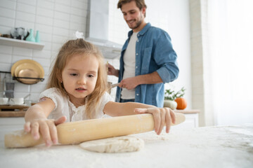 Caring young Caucasian father and cute little preschooler daughter bake in kitchen at home together