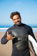 Portrait of happy bearded surfer posing with surfboard and smiling. Handsome brunette active man...