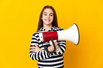 Little girl isolated on yellow background holding a megaphone and smiling