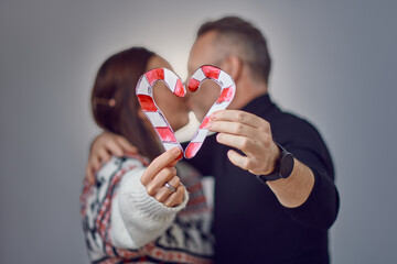 Incognito married adult couple kissing and showing the heart-shaped figure of candy canes candies. Christmas holiday loving family portrait in studio