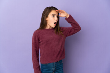 Little girl isolated on purple background with surprise expression while looking side