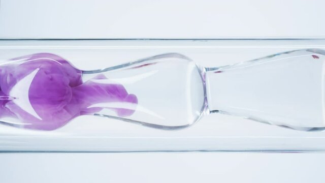 Pink liquid substance flows through a glass flask. Concept for advertising perfume and cosmetic products. Mixing pink ink with water in a large laboratory glass test tube.