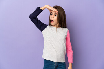 Little girl isolated on purple background doing surprise gesture while looking to the side