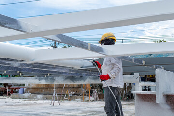 The painter is working to fireproof paint on steel structure with spray gun, at industrial factory.