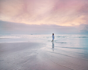 Woman wearing a casual dress is walking on a beautiful sandy beach during colorful vibrant  pink summer sunset. Thailand. Meditation, solitude, tranquility concept 