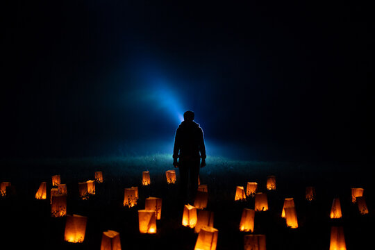 Silhouette of a young man standing in the middle of a  night green grass field covered with paper lanterns. Make A Wish.  A Chinese lanterns  in the background. Fantastic background image 