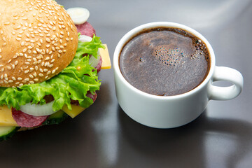 Hamburger with vegetables and sausage and coffee on a gray background. Fast food and breakfast. Calories and diet.