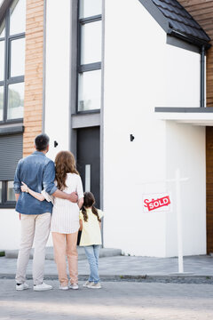 Full Length Of Daughter Standing Near Father And Mother Hugging Near House And Sign With Sold Lettering