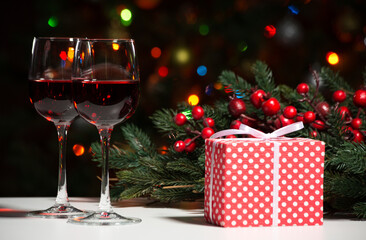 Glasses of wine and Christmas gift and balls on the background of Christmas lights and Holly red berries
