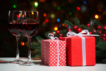 Glasses of wine and Christmas gifts and balls on the background of Christmas lights and Holly red berries