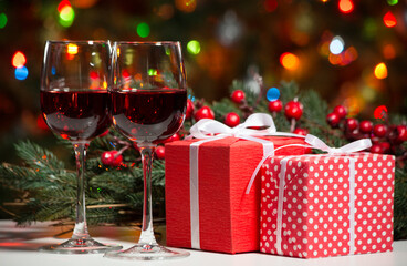 Glasses of wine and Christmas gifts and balls on the background of Christmas lights and Holly red berries