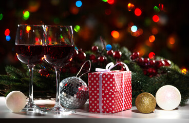Glasses of wine and Christmas gift and balls on the background of Christmas lights and Holly red berries