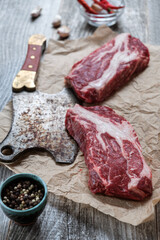 Two beef steaks, an old meat axe and spices on a wooden background.