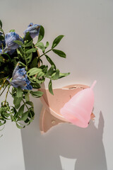 pink menstrual cup with flowers on white background with sunlight and shadows