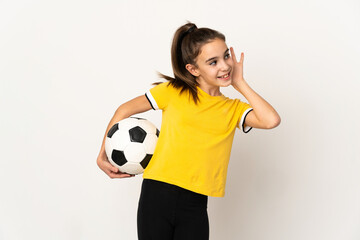 Little football player girl isolated on white background listening to something by putting hand on the ear