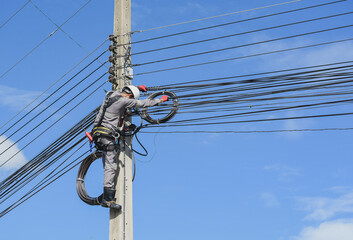 Electrical wireman repair Power cable wearing safety full harness on blue sky