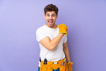 Young electrician man over isolated on purple background celebrating a victory