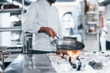 Frying pan is on fire. Chef in white uniform cooking food at kitchen. Busy day at work