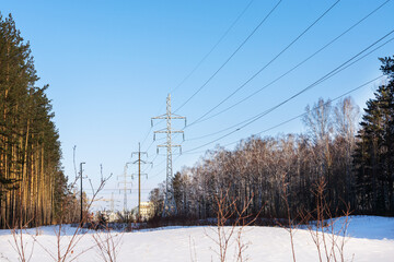 The power transmission line is located in a winter forest between pines and birches